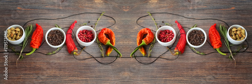 Fototapeta Concept of hot spice cuisine and seasoning - peppers, herbs, condiment. Black pepper, pink pepper, cardamon seeds, thyme, rosemary and chili peppers on wooden table. Wide panorama, horizontal