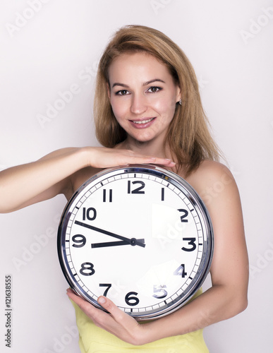 Poster Beautiful young woman looking at a large silver retro clock that she is holding,