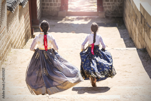 Poster Two Korean Girls dressed in traditional dress running down stairs in Seoul stree