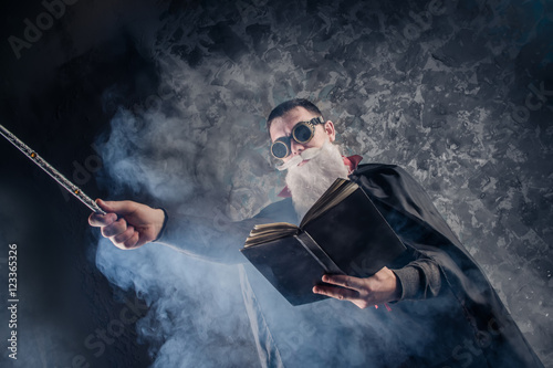 Poster evil wizard Merlin conjures and casts a spell, raising his wand, a young man dre