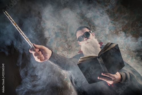 Poster evil wizard Merlin conjures and casts a spell, raising his wand, a young man dre