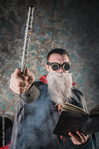 Poster evil wizard Merlin conjures and casts a spell, raising his wand, a young man dre