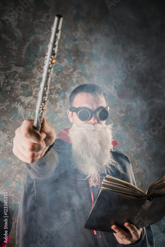 Poster evil wizard Merlin conjures and casts a spell, raising his wand, a young man dre