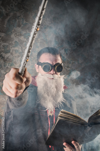 Poster evil wizard Merlin conjures and casts a spell, raising his wand, a young man dre