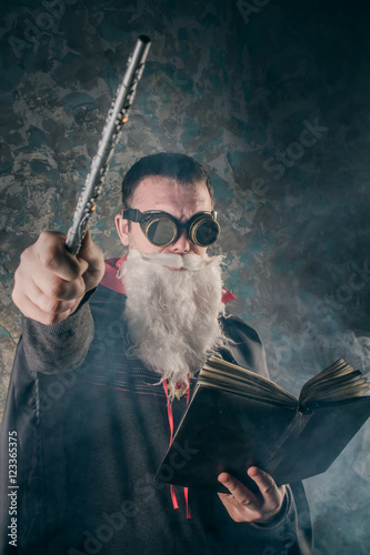 Poster evil wizard Merlin conjures and casts a spell, raising his wand, a young man dre