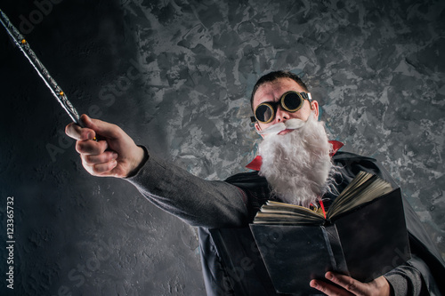 Poster evil wizard Merlin conjures and casts a spell, raising his wand, a young man dre