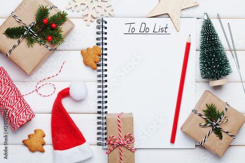 Poster Holiday decorations, gift, present box, miniature fir tree and notebook with to do list on white wooden table from above