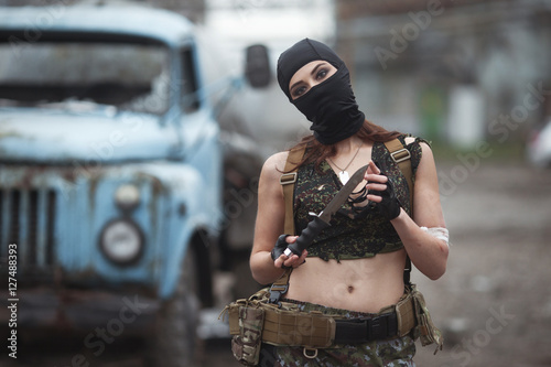 Poster девушка в военной форме с ножом в маске в условиях боевых действий , на заднем ф