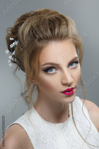 Elegant bride with a beautiful hairstyle and bright make-up isolated on a gray background. © ksi