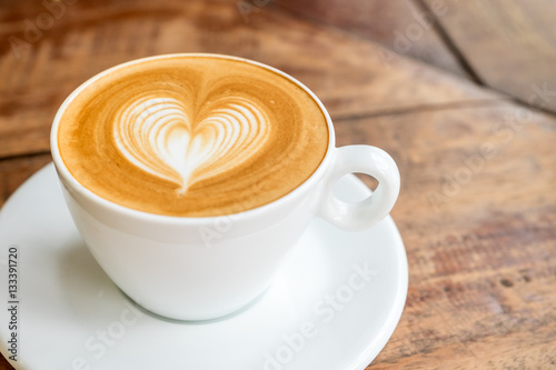 Close up white coffee cup with heart shape latte art on wood tab