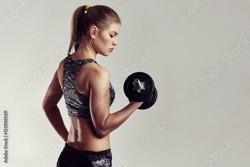 Studio portrait of athletic woman holding dumbbell, improving her arm muscles and body. Copy space on background. 