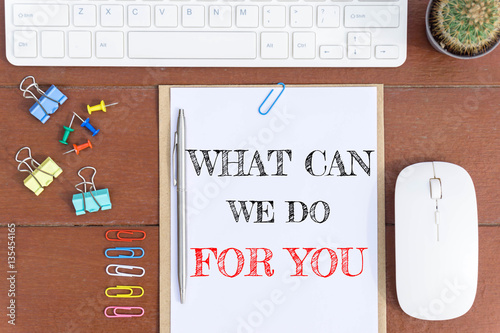 Poster Text What can we do for you on white paper which has keyboard mouse pen and office equipment on wood background / business concept