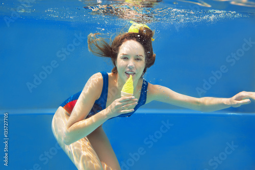 Poster Beautiful smiling red hair girl eating yellow ice cream in the swimming pool und
