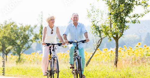 Senioren, Paar aus Frau und Mann, fährt Fahrrad an einem Sonnenblumen Feld