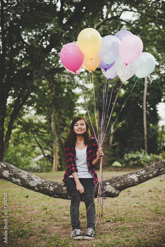 Poster Young hipster woman sitting on tree branch with colorful of balloons in hand, Relaxing enjoy holiday