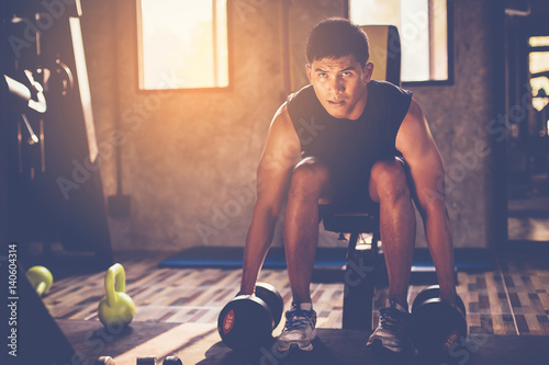 Poster Portrait of a male muscular bodybuilder workout with dumbbell in fitness gym