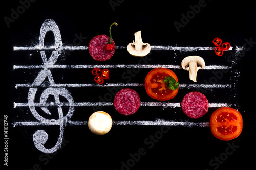  Concept of cooking pizza, like notes from ingredients. Salami, tomato and mozzarella cheese on a black background with a treble clef.