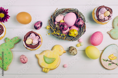 Poster Easter nest cupcakes, painted eggs and ginger breads on light wooden background