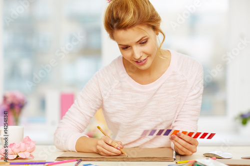Poster Pretty young interior designer sketching with pencil while holding color swatch