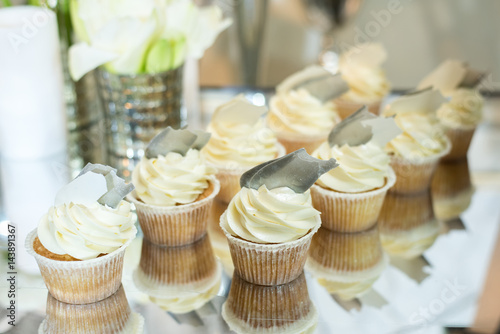 Poster Cupcakes with white cream on the table decorated with white flowers and candles