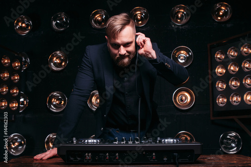Poster Young disk jockey with headphones and mixer checking equipment