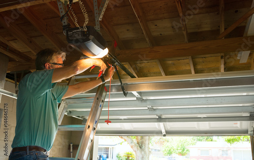 Professional automatic garage door opener repair service technician man working on a ladder at a home residential location making adjustments and fixing it while installing it. © mokee81