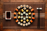 Japanese food art. Delicious uramaki rolls set, colorful round ornament of sushi served on brown straw mat, flat lay. Luxury restaurant menu photo.