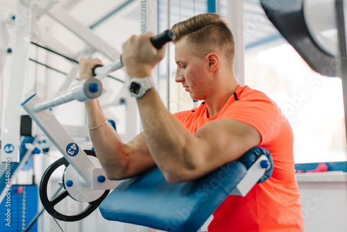 Poster young attractive athletic guy training his biceps looking at it