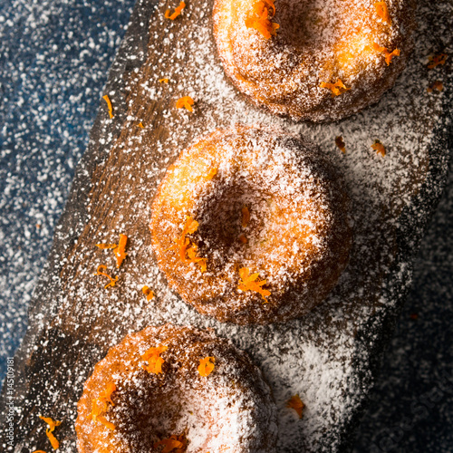 Poster Mini bundt ring cakes with orange zest icing sugar on dark blue background and serving board