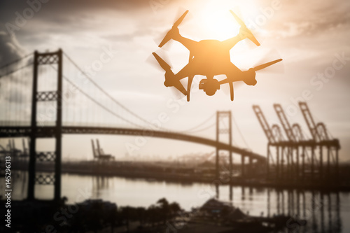 Silhouette of Unmanned Aircraft System (UAV) Quadcopter Drone In The Air Over Shipping Port.