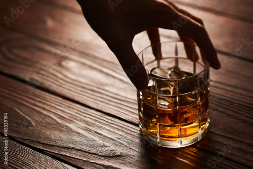 Glass of whiskey with ice cubes on wooden table