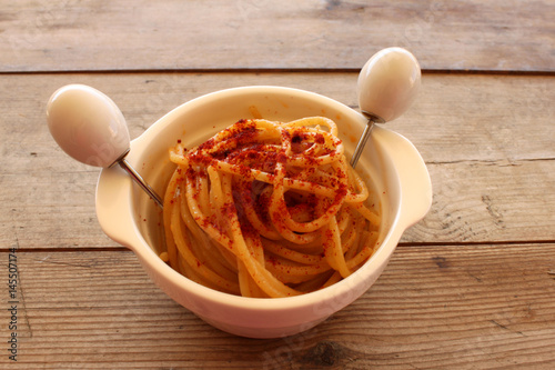 Poster pasta aglio,olio e peperoncino piccante in pentola bianca su tavolo di legno
