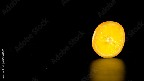 rolling orange fruit slice on black background, slow motion