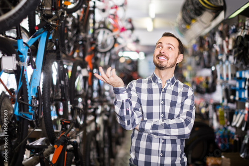 joyous man in bicycle shop chooses for himself sports bike