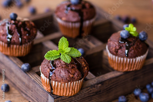 Poster Chocolate muffins with chocolate syrup, blueberries and mint in a wooden backgro