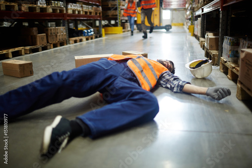Fallen worker lying on the floor in aisle between storage shelves © pressmaster