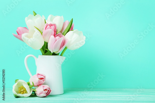 Bouquet of tulips in jug on green background