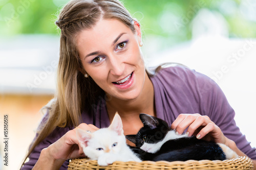 Poster Portrait of happy young woman stroking cute kittens in basket looking in camera
