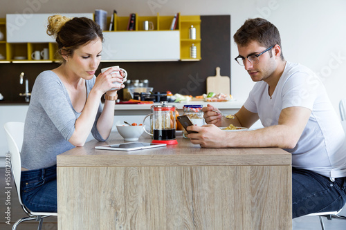 Poster Beautiful young couple using digital tablet and smartphone while enjoying the breakfast