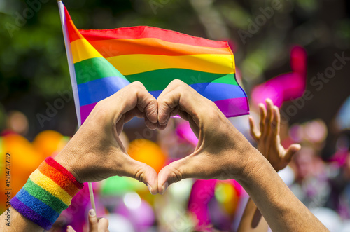 Poster Supporting hands make heart sign and wave in front of a rainbow flag flying on t