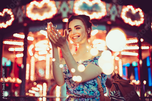 Beautiful young woman smiling and talking garlands of lights at city