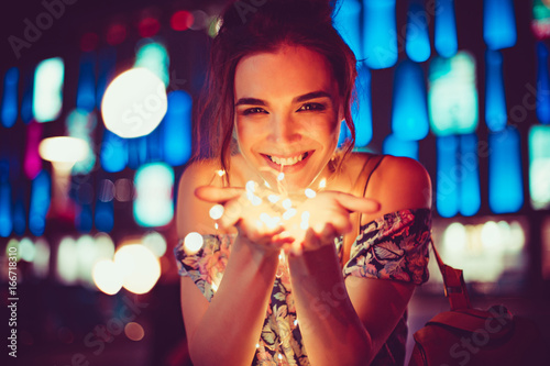 Beautiful young woman smiling and talking garlands of lights at city