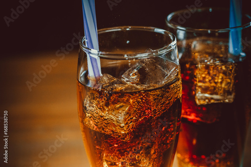 Beautiful cold drink of Cola with ice cubes with a boiler straws in glasses on w Poster