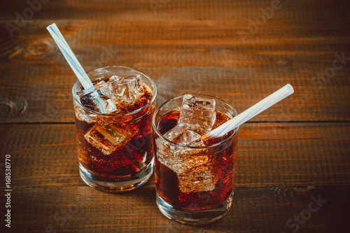 Beautiful cold drink of Cola with ice cubes with a boiler straws in glasses on w Poster