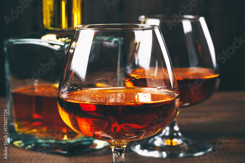 Two glasses of brandy or cognac and bottle on the wooden table.