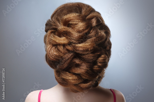 Beauty portrait of a girl with a voluminous hairdo from the back against a gray background. © ksi