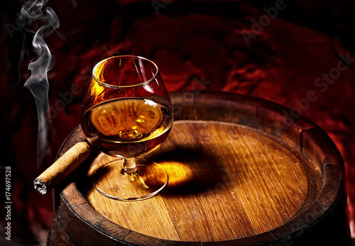 Cognac and Cigar on old oak barrel.Red stone background