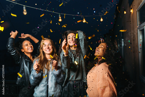 Night party on a terrace. Happy women having fun under confetti.