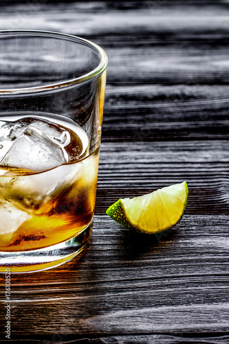rum with ice in glass on dark background and lime