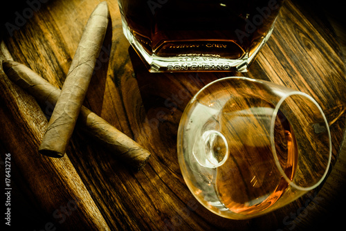 Top view of two cigars, a glass and a bottle of rum on a wooden surface